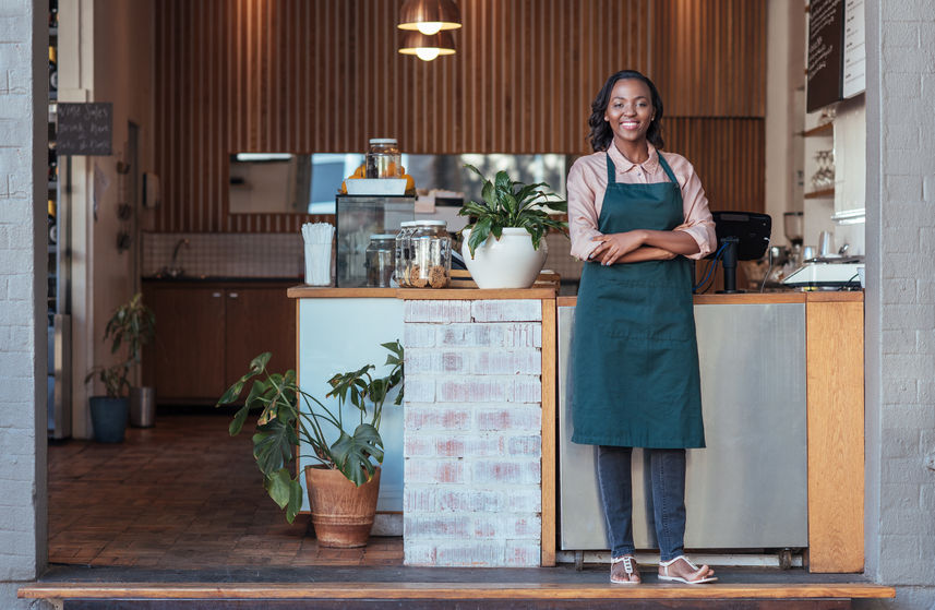 smiling woman entrepreneur standing welcomingly in front of her cafe